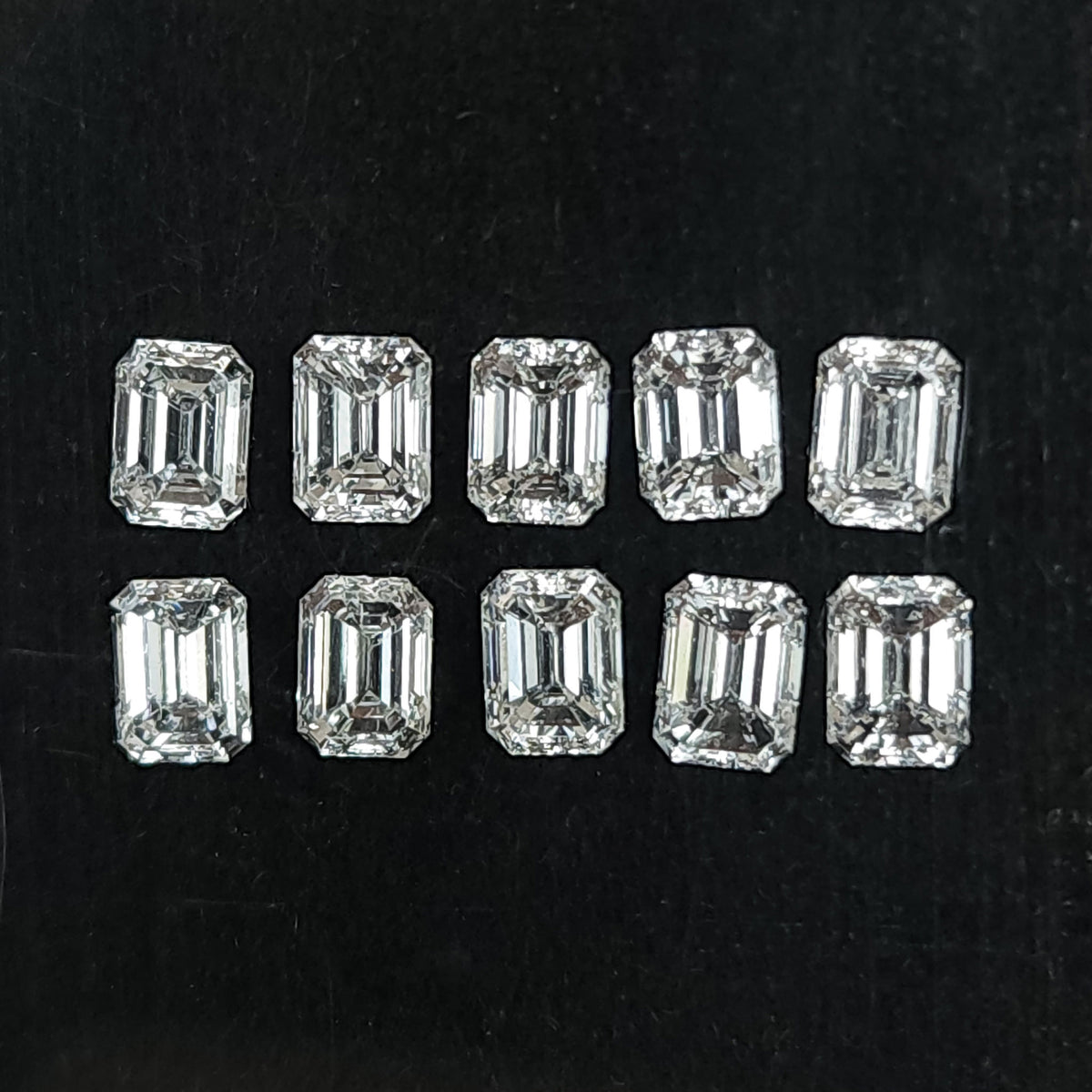 Ten representative emerald-cut diamonds arranged crown-up in two rows on black backing; sold per stone.