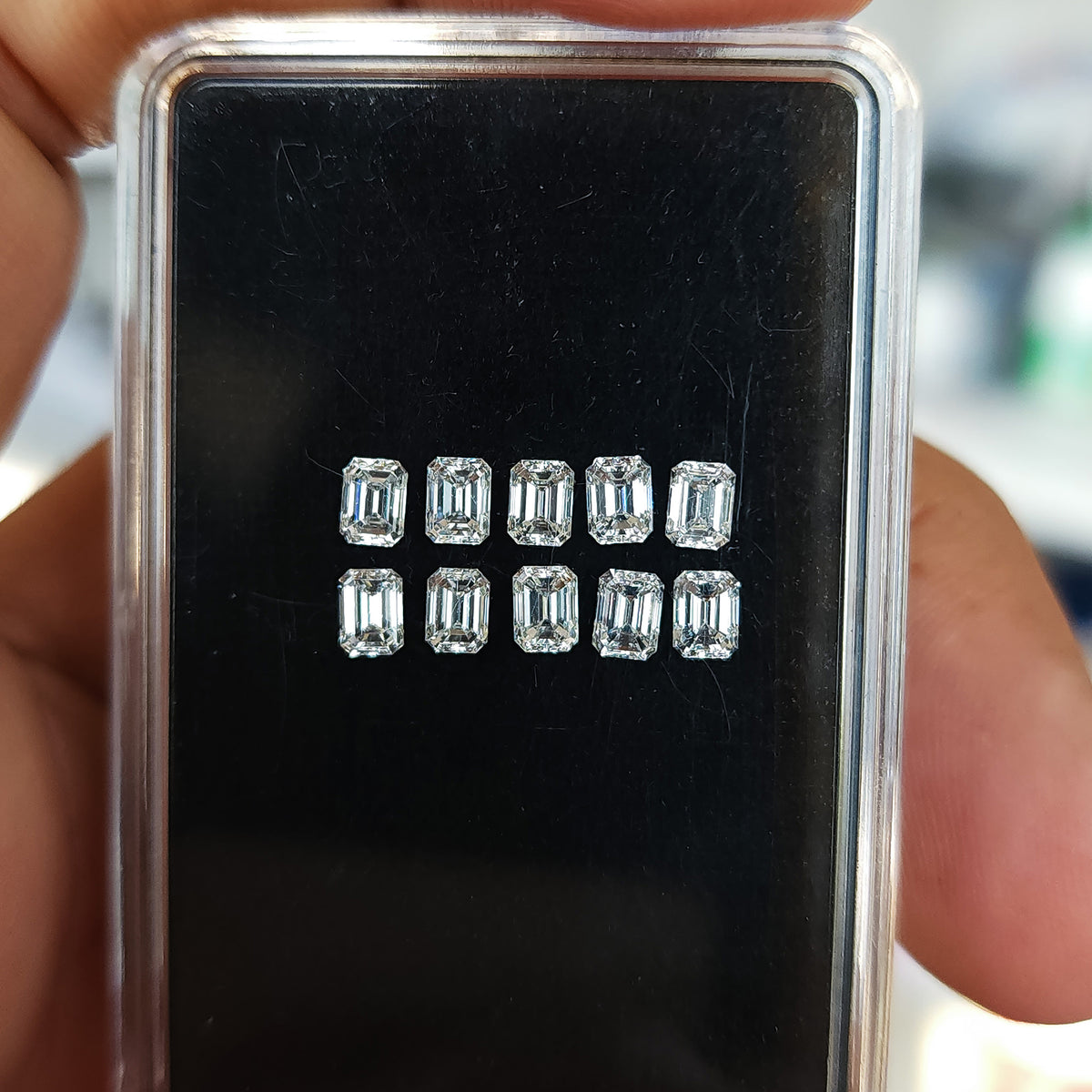 Close hand-held view of ten emerald-cut diamonds arranged crown-up inside a black display case.