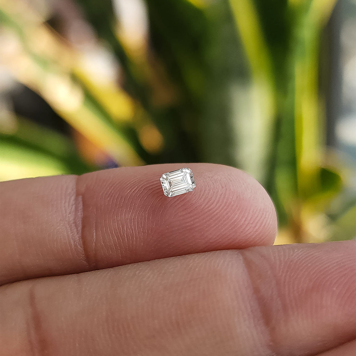 Emerald-cut diamond shown on a fingertip from an alternate crown-up angle for scale.