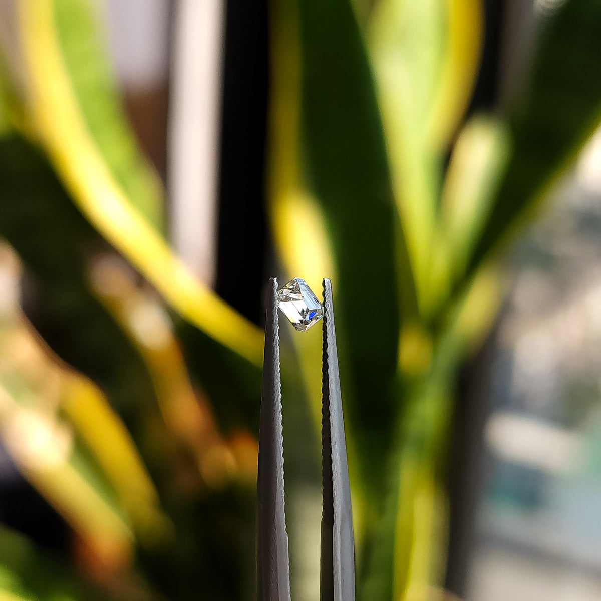 Side-profile view of a rectangular emerald-cut diamond in tweezers, showing crown and pavilion depth.