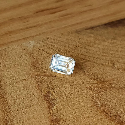 Single rectangular emerald-cut diamond lying crown-up on a wooden surface, with its step pattern visible.
