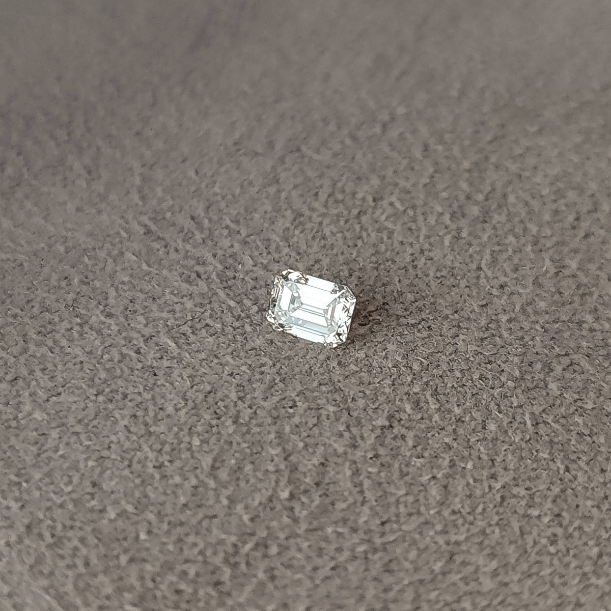 Single emerald-cut diamond lying crown-up on gray fabric with bright table reflections.