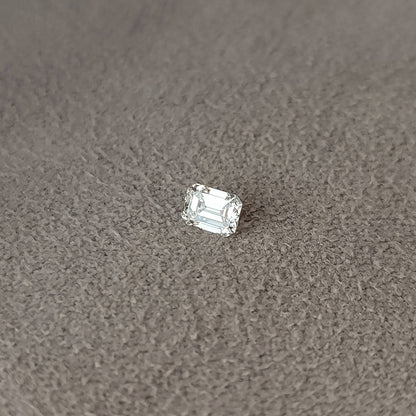 Single emerald-cut diamond lying crown-up on gray fabric with bright table reflections.