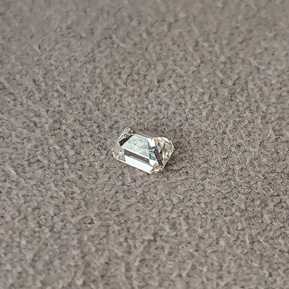 Oblique reverse view of a rectangular emerald-cut diamond on gray fabric, showing pavilion facets.