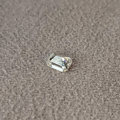 Oblique reverse view of a rectangular emerald-cut diamond on gray fabric, showing pavilion facets.