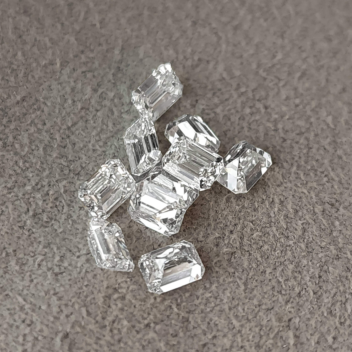 Group of loose emerald-cut diamonds on gray fabric in mixed crown, side and pavilion orientations.