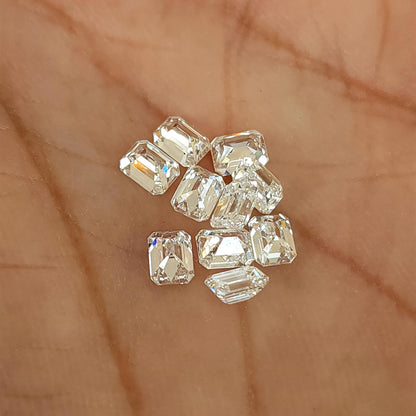 Loose emerald-cut diamond stock resting in a palm in mixed crown and pavilion orientations; sold per stone.