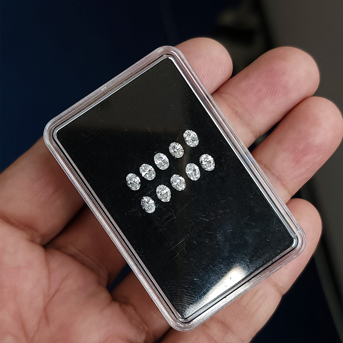 Black diamond display box tilted across a hand, showing two rows of oval diamonds.