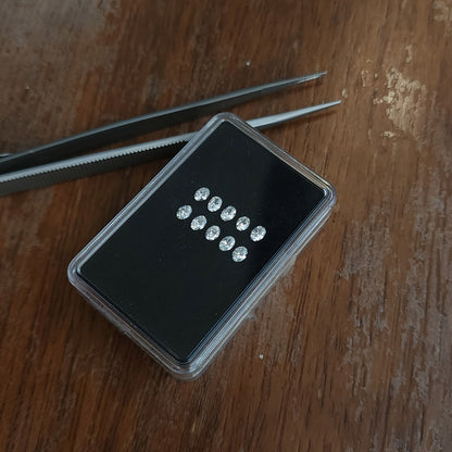 Display box of oval diamonds resting on a wooden surface beside tweezers.