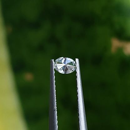 Reverse view of an oval diamond in tweezers, showing pavilion facets against a green background.