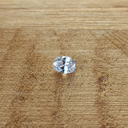 Single oval brilliant diamond lying face-up on a wooden surface.