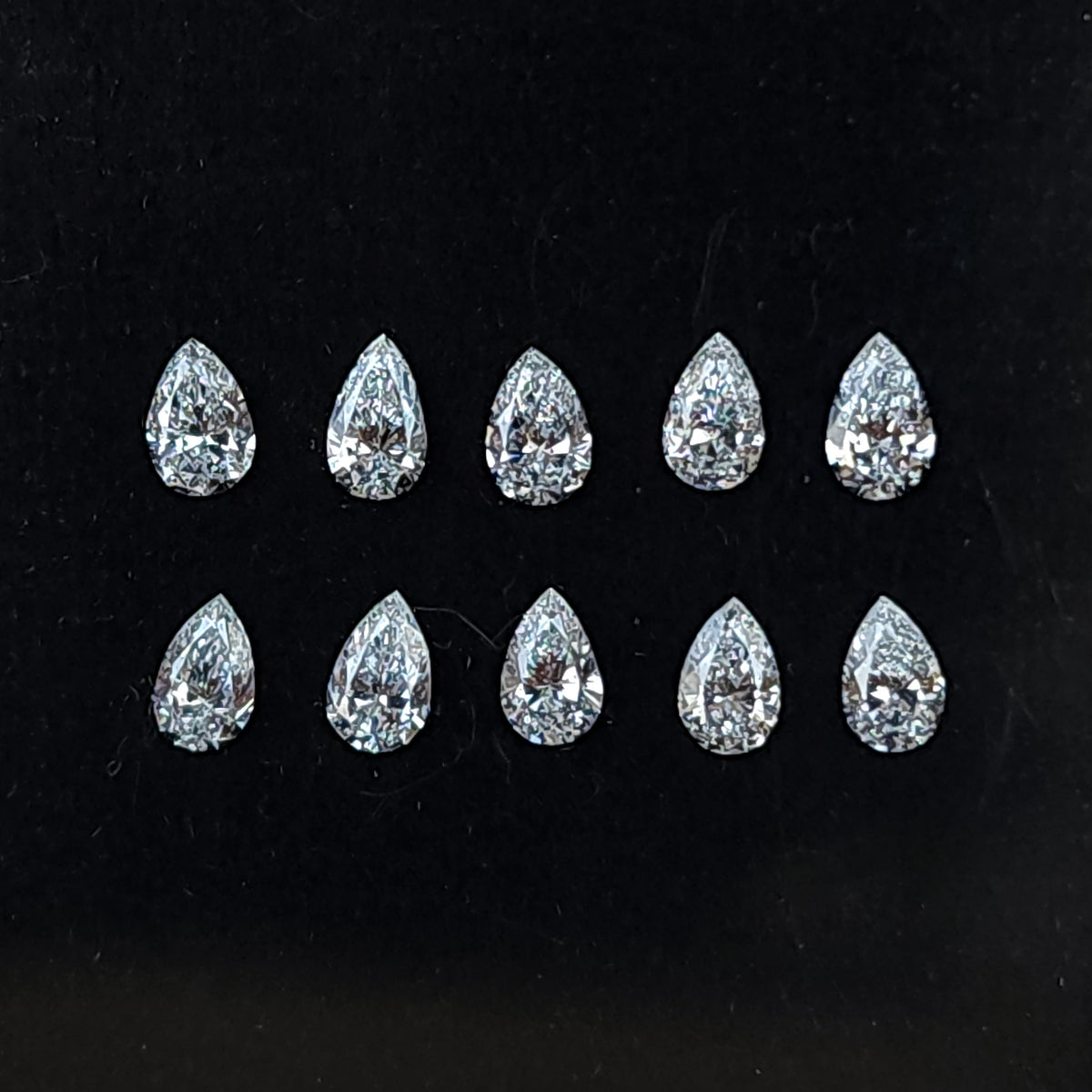 Ten representative pear brilliant diamonds arranged crown-up in two rows on black backing; sold per stone.