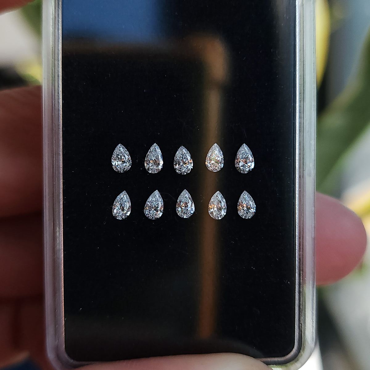 Black display case of crown-up pear brilliant diamond stock held with fingers visible around the case.