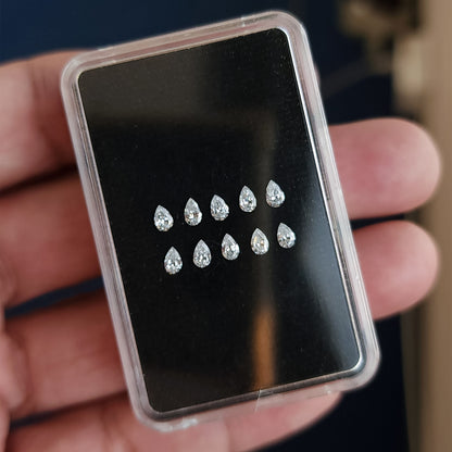 Hand holding a black display box containing two rows of representative pear diamond stock.