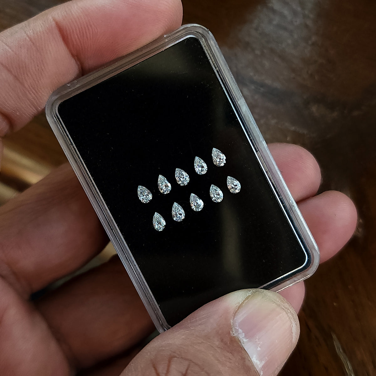 Angled hand-held display case showing representative pear brilliant diamonds arranged crown-up.