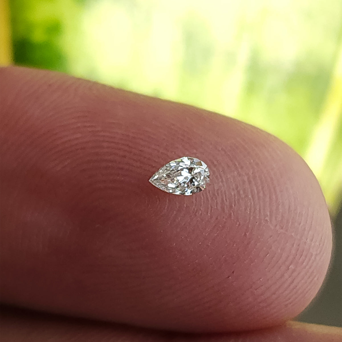 Single pear brilliant diamond resting crown-up on a fingertip for scale against a green background.