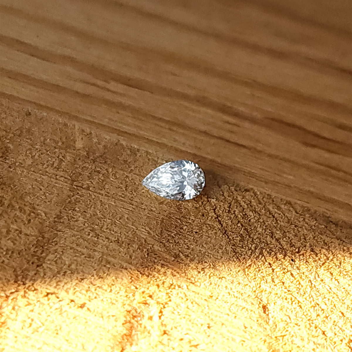 Single natural pear brilliant diamond lying crown-up on a wooden surface, showing its point, rounded end and table.