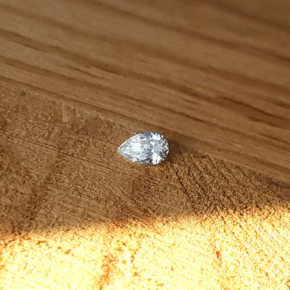 Single natural pear brilliant diamond lying crown-up on a wooden surface, showing its point, rounded end and table.