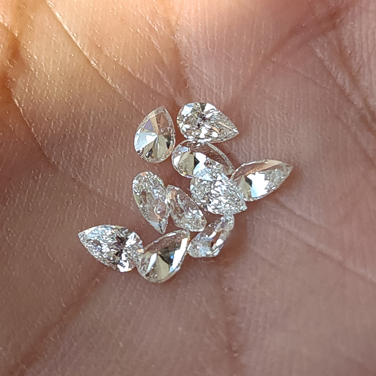 Loose pear brilliant diamond stock resting in a palm in mixed crown and pavilion orientations; sold per stone.