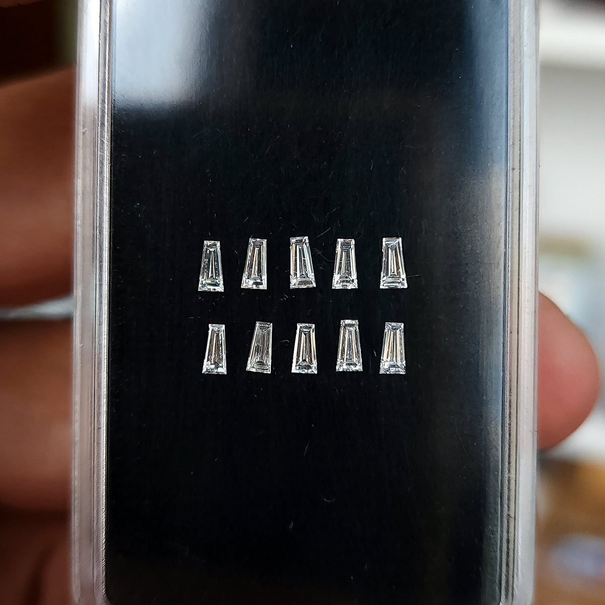 Diamantes baguette trapezoidales dispuestos en dos filas en una caja de exhibición forrada en negro, vistos desde un ligero ángulo.