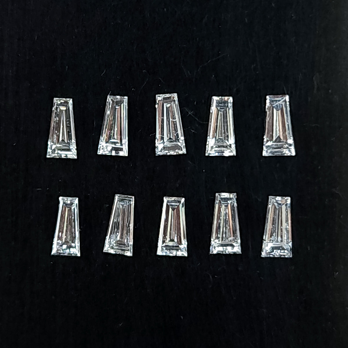 Diamantes naturales baguette trapezoidales dispuestos en dos filas sobre un cojín negro, mostrando tablas planas transparentes y facetas escalonadas.