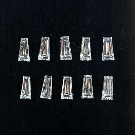 Natural tapered baguette diamonds arranged in two rows on a black cushion, showing transparent flat tables and step facets.