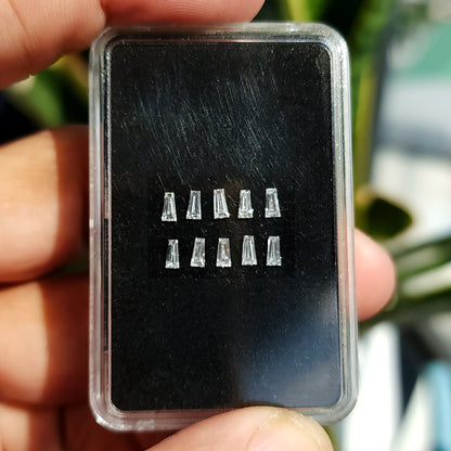 Una caja transparente para gemas sostenida por los dedos, conteniendo dos filas de diamantes baguette trapezoidales sobre un cojín negro.