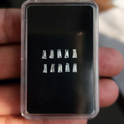 Diamantes baguette trapezoidales sobre una almohadilla negra en una caja transparente sostenida por una mano.