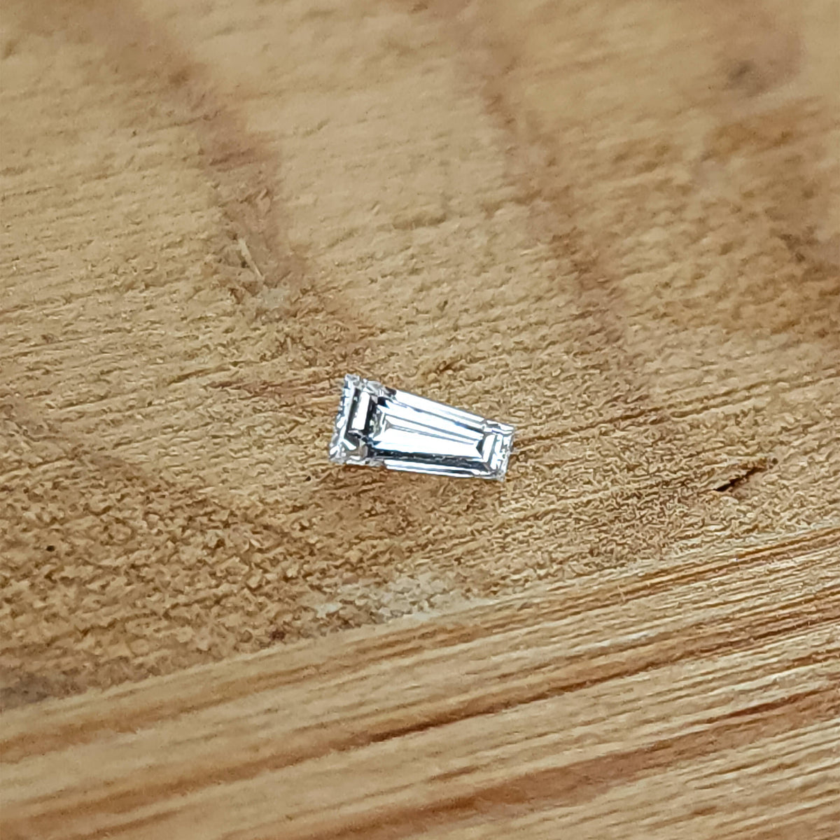 Un diamante baguette trapezoidal sobre madera, con un reflejo brillante en la cara central.