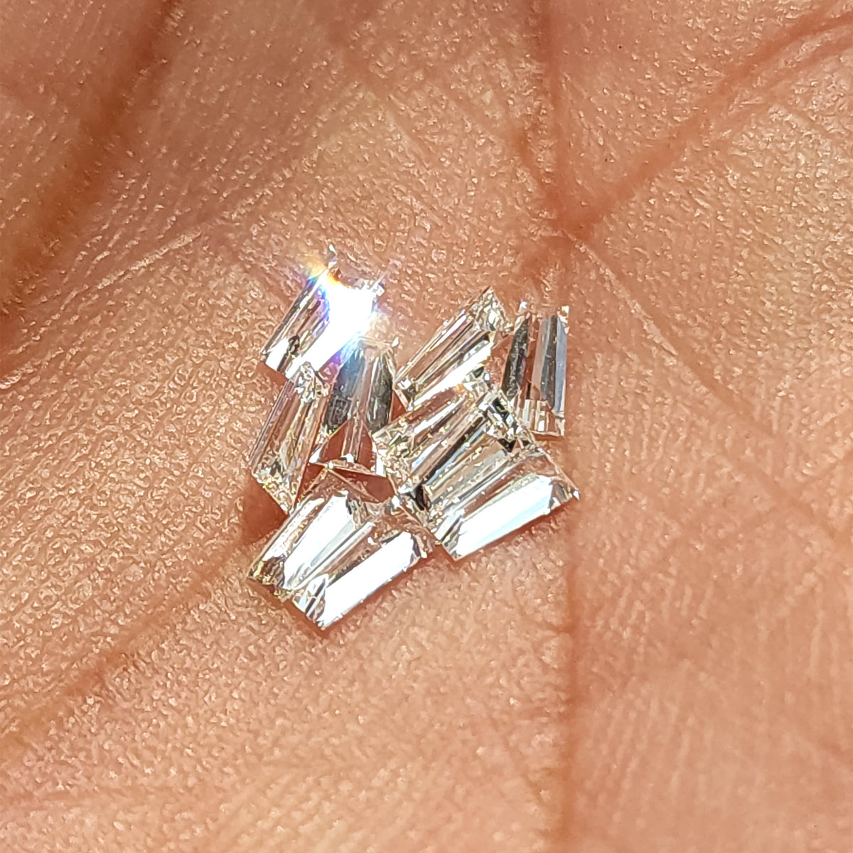 Diamantes baguette trapezoidales agrupados sobre la piel, con reflejos fuertes y brillantes a través de varias piedras.