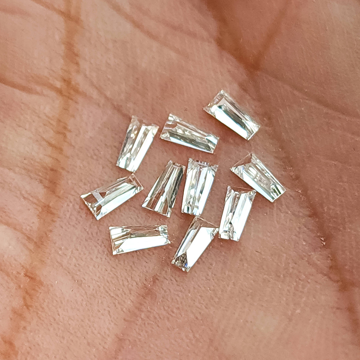 Diamantes baguette trapezoidales sueltos en una palma, mostrando sus caras transparentes estrechas y reflejos puntiagudos.