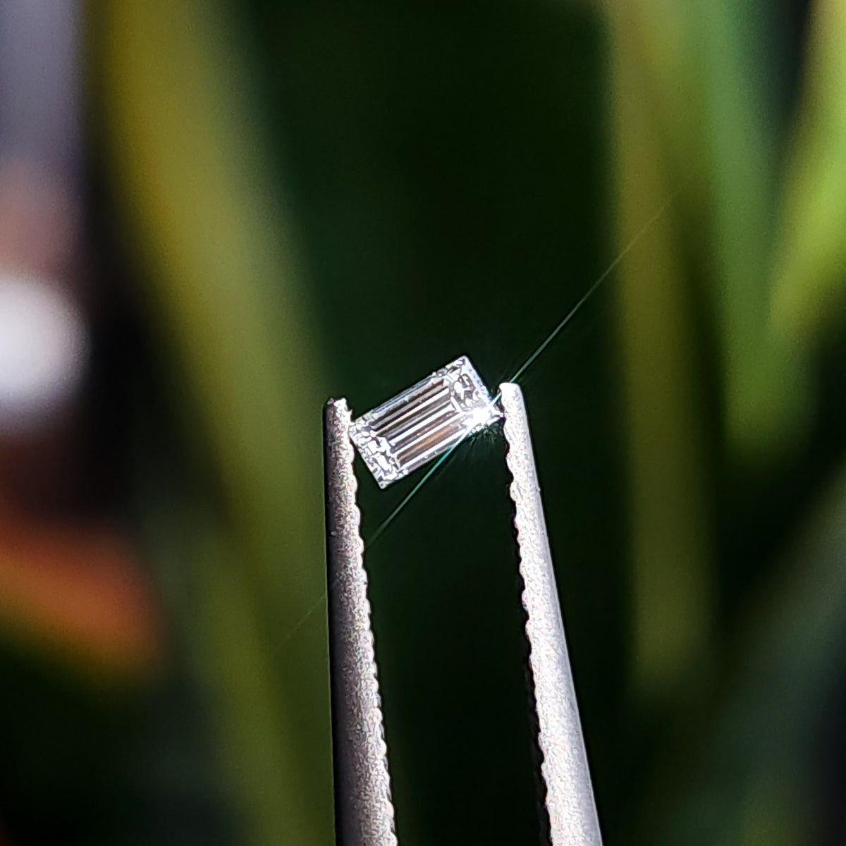 Side and profile view of one natural baguette step-cut diamond held in tweezers.