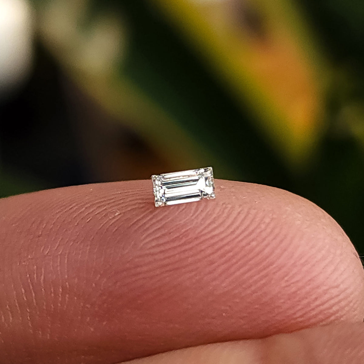 One small natural baguette step-cut diamond on a fingertip for scale.