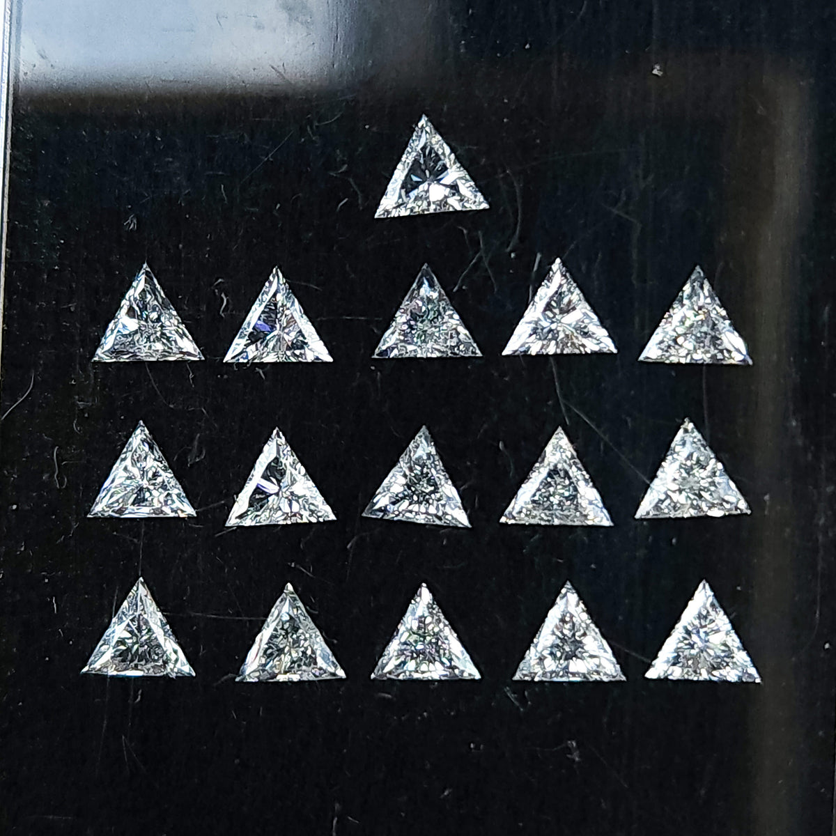 Close face-up group of triangle diamonds in a black display box, with pointed outlines and brilliant facets visible across the parcel.