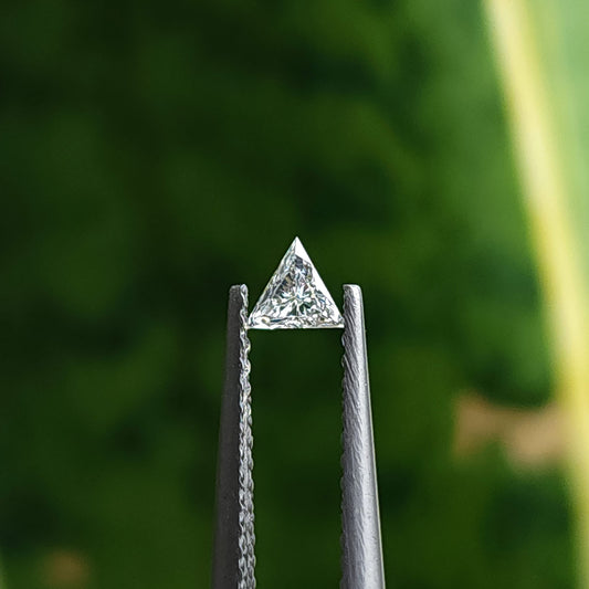 One triangle diamond held face-up between vertical tweezers against a green background, showing its full three-sided outline and brilliant facets.