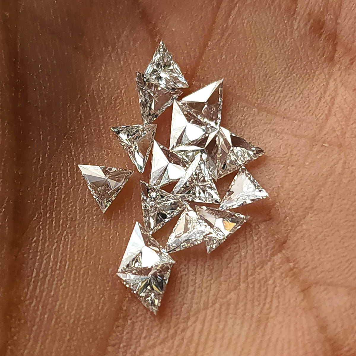 Loose triangle diamonds scattered in a palm at varied angles; stock reference only, with purchase price applying to one diamond.
