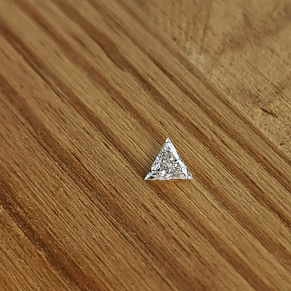 One triangle diamond lying face-up on a light wooden surface, showing its three points and bright crown facets.