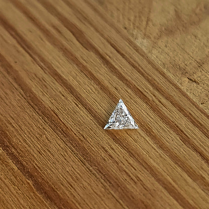 One triangle diamond lying face-up on a light wooden surface, showing its three points and bright crown facets.