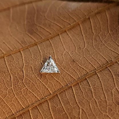 Single triangle diamond on a textured tan surface, with bright white reflections against the warm background.