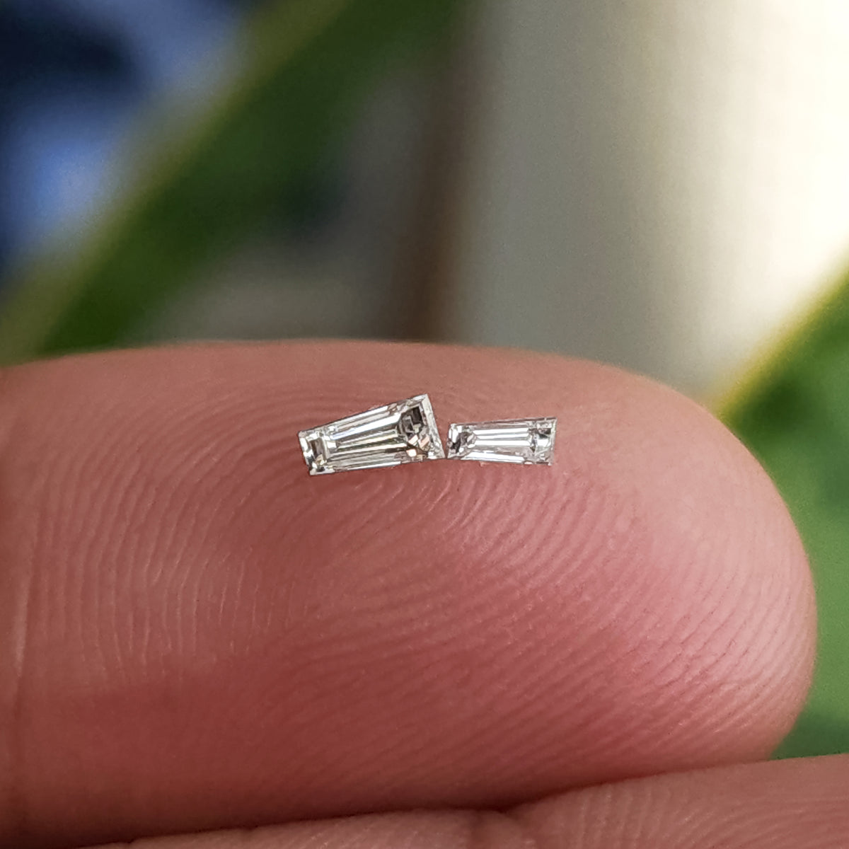 Dos diamantes baguette trapezoidales de diferentes tamaños descansando sobre la punta de un dedo para escala relativa.