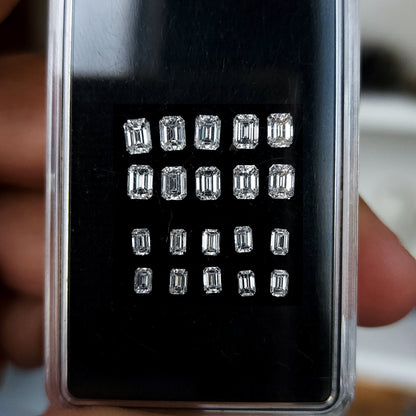Representative emerald-cut diamond stock arranged crown-up in upper and lower size groups inside a black case.