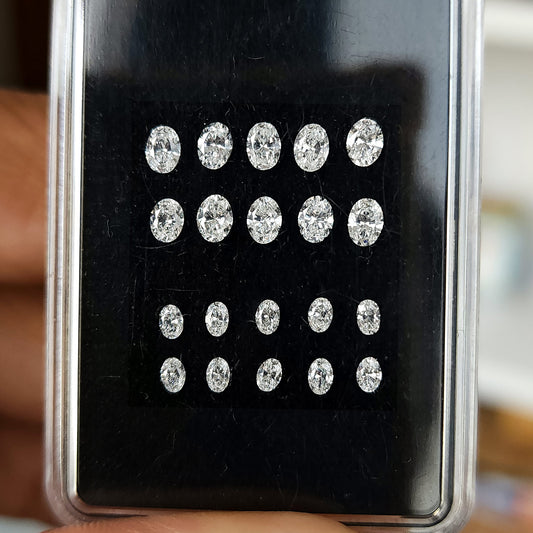 Natural oval brilliant diamonds in two size groups arranged face-up in a black display box.