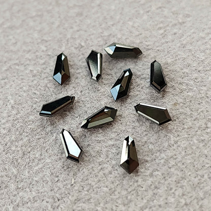 Ten black shield-shaped diamonds scattered on gray textured paper, with bright reflections along their edges.