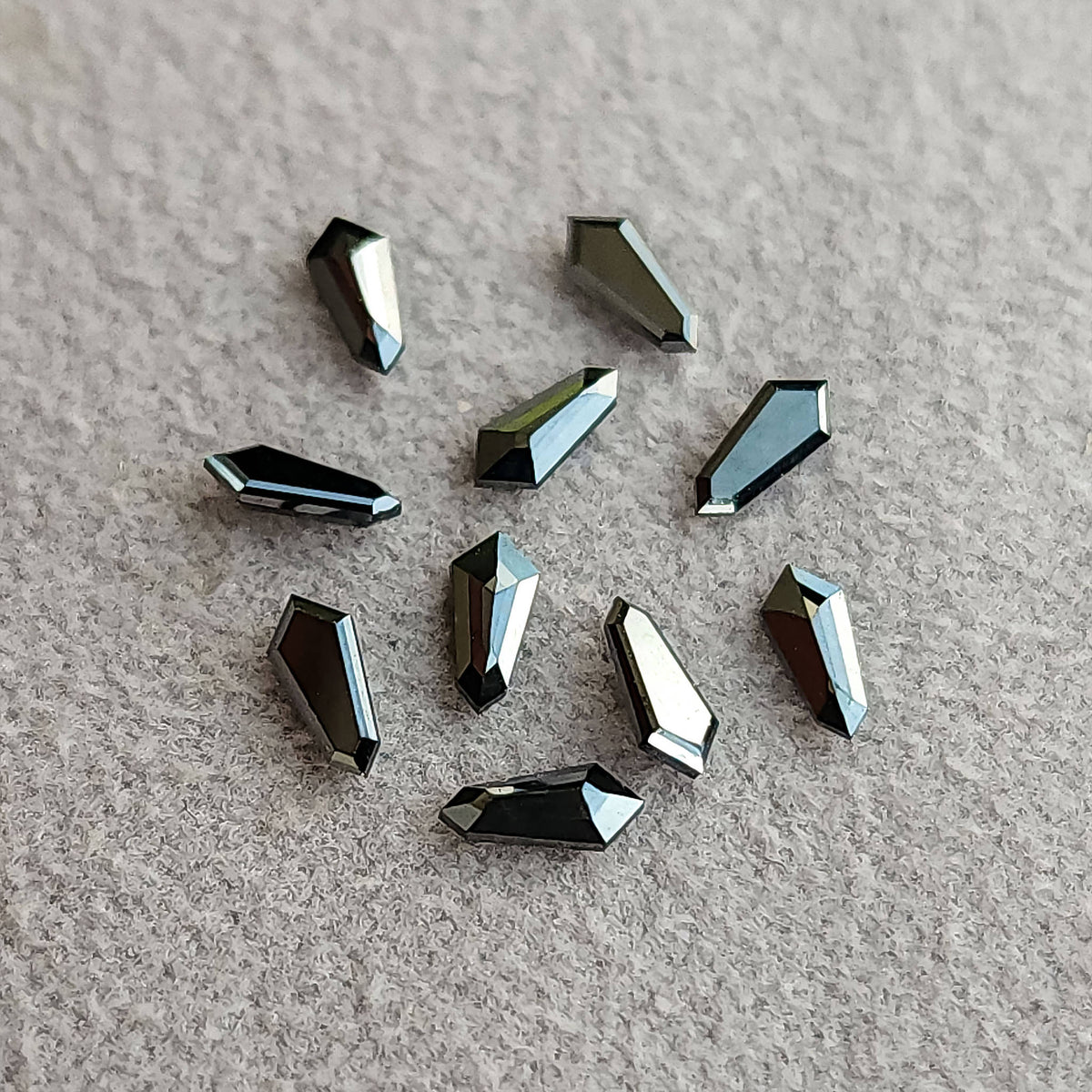 Alternate arrangement of ten black shield diamonds on gray paper, with light and dark facet reflections.