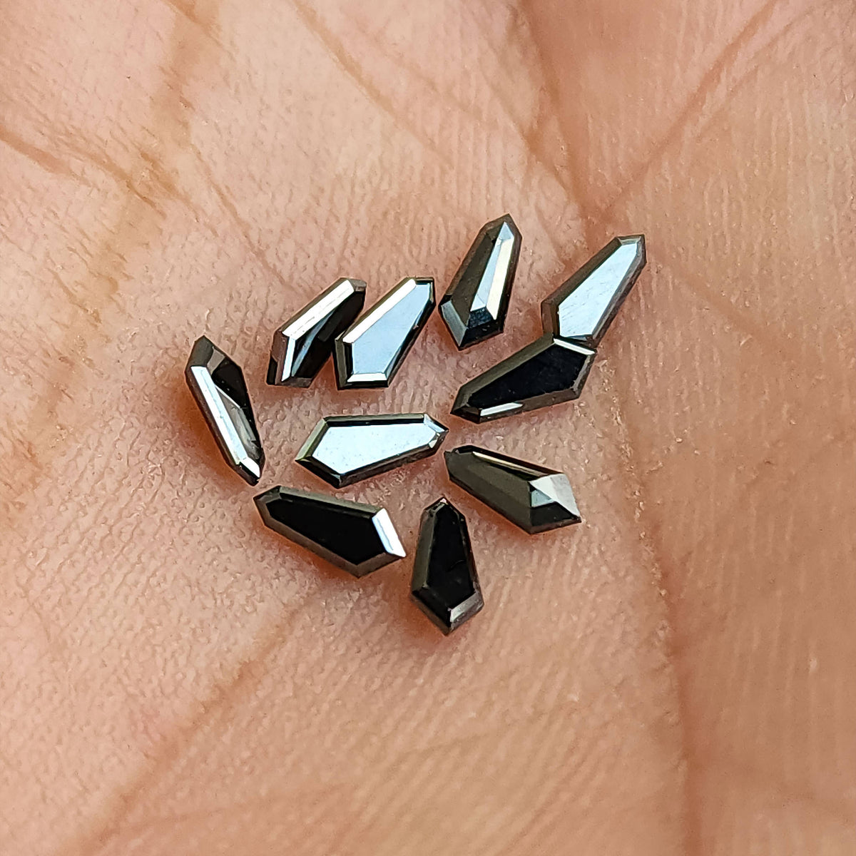 Black shield-shaped diamonds spread on a hand, showing their small calibrated size and reflective edges.