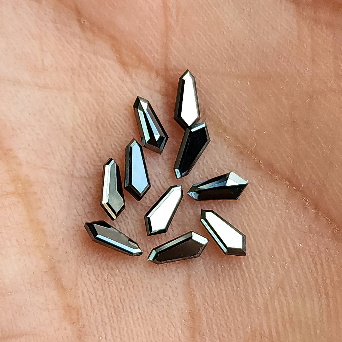 Group of black shield diamonds in a palm, with strong white and blue-gray reflections across angled facets.