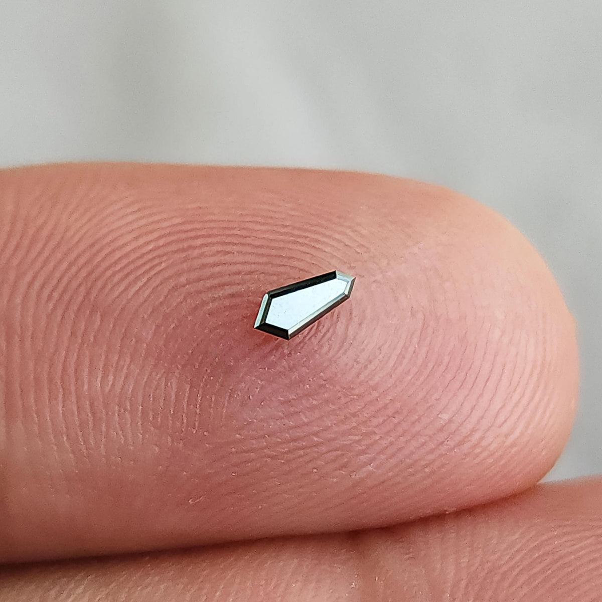 Single shield diamond on a fingertip at a brighter angle, with its face reflecting pale light.