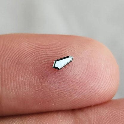 Single shield diamond on a fingertip at a brighter angle, with its face reflecting pale light.