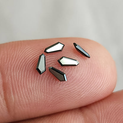 Several black shield diamonds on a fingertip, illustrating scale and variation in reflected light; sold per piece.