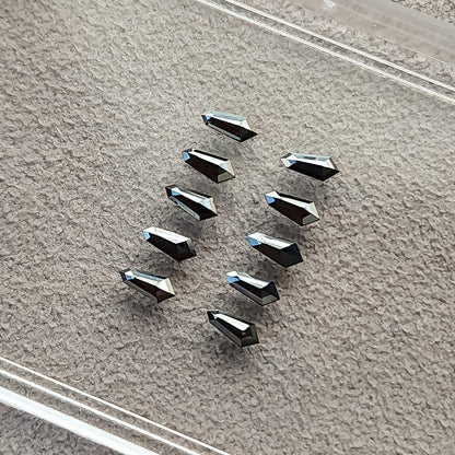 Ten black shield diamonds arranged on gray paper beneath a clear display-box lid, with alternating reflective faces.